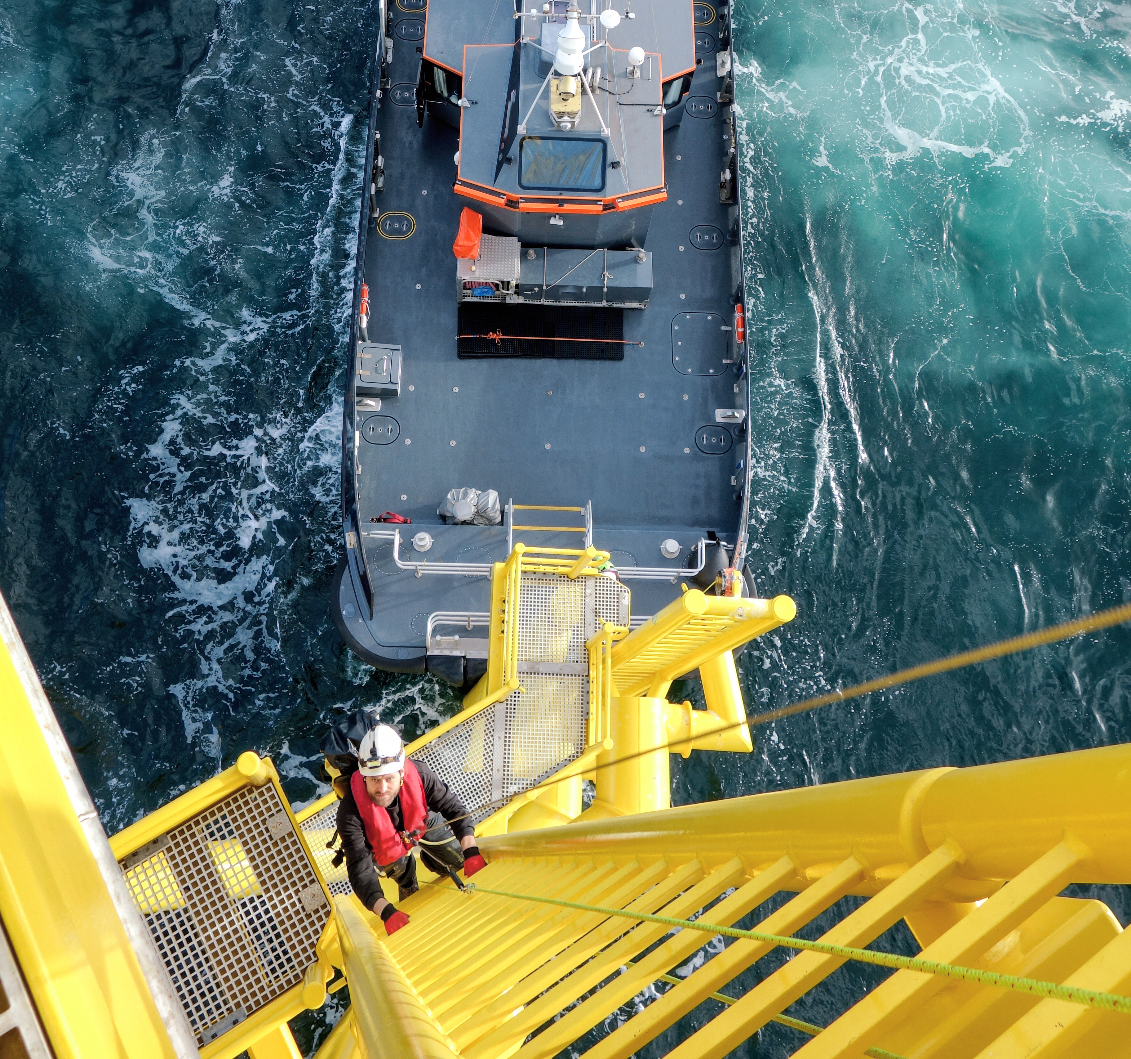 An aerial view of a person in a hard hat climbing a boat landing's ladder, with a vessel pressed against the bottom of the landing.